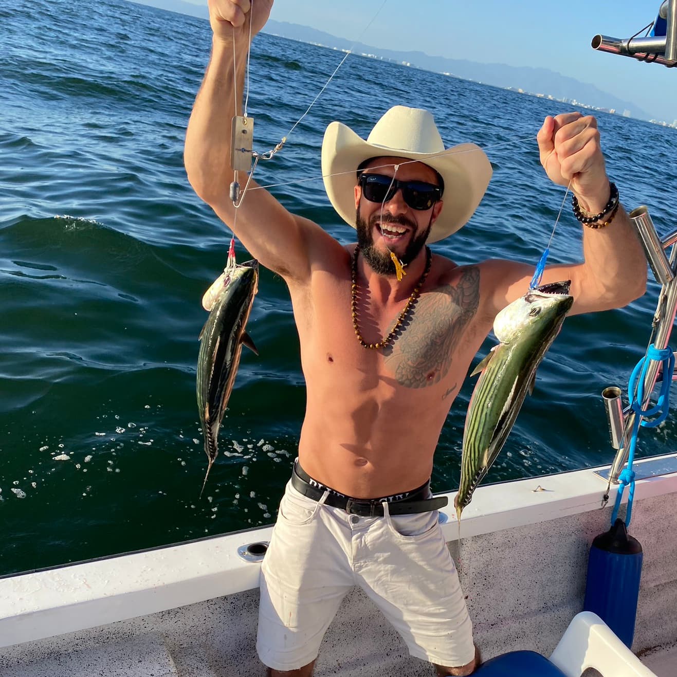 Un pescador muestra dos peces en una lancha frente a la costa